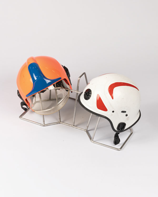 Support pour ARI et casques avec deux casques de pompier — un orange avec des détails bleus, un blanc avec du rouge et du noir — sur un rack en métal.