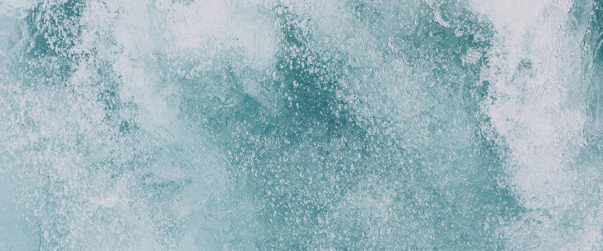 Aerial view of turbulent blue water with swirling patterns and foam in various shades of blue and white.