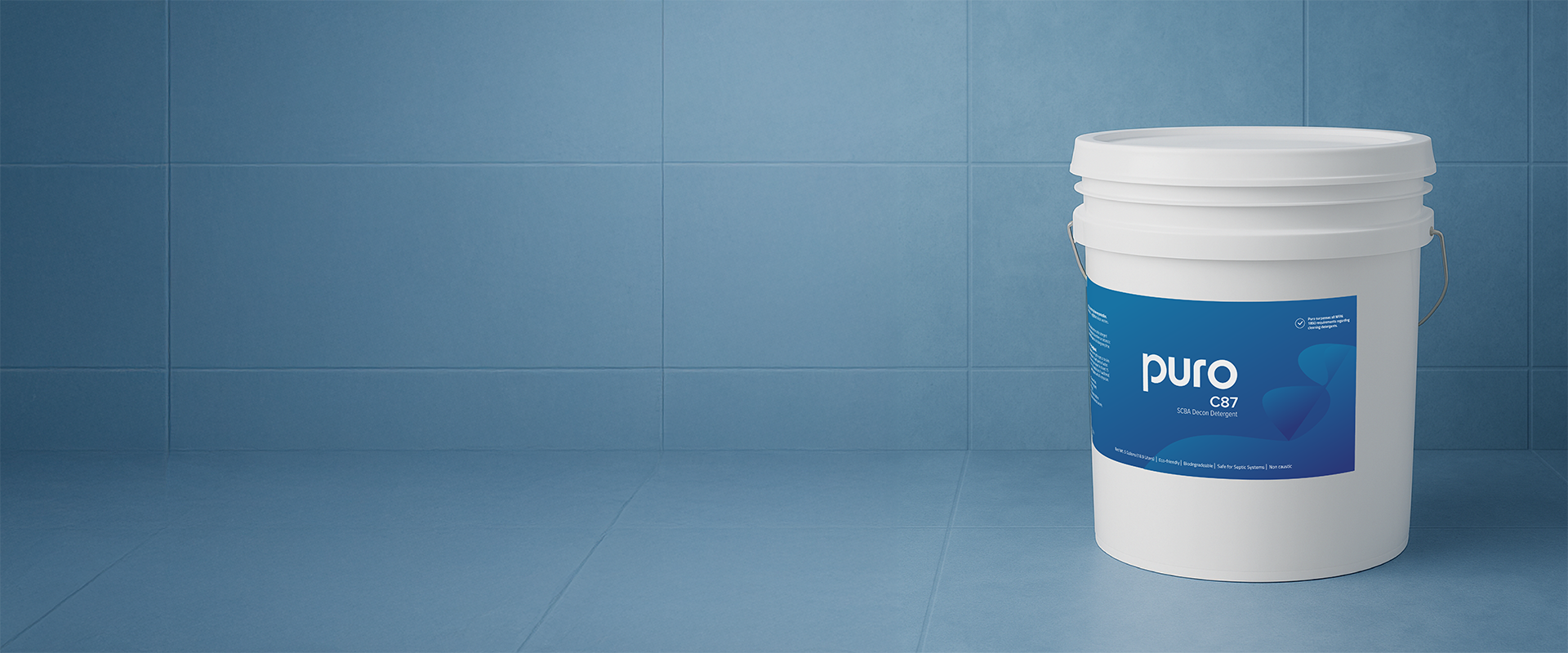 White bucket of Puro C87 SCBA decontamination detergent placed on a blue tiled floor and wall background.