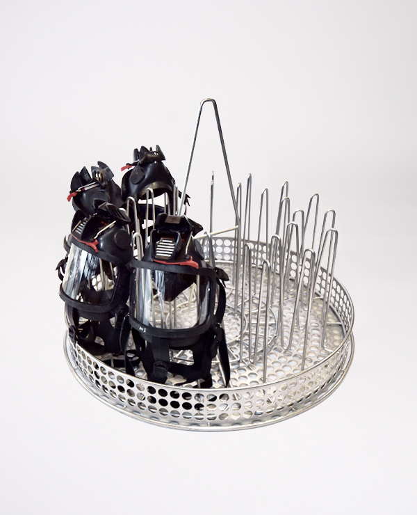 Utrustningshållare med skyddsmasker placerade i en perforerad rund korg med avdelare för dekontaminering.