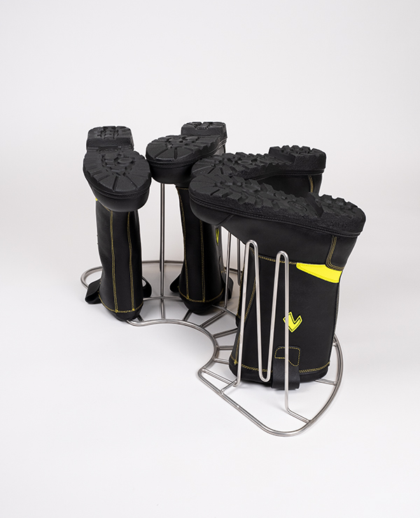 Utrustningshållare med två par svarta stövlar placerade upp och ner, säkrade i metallfästen, med sulorna uppåt.