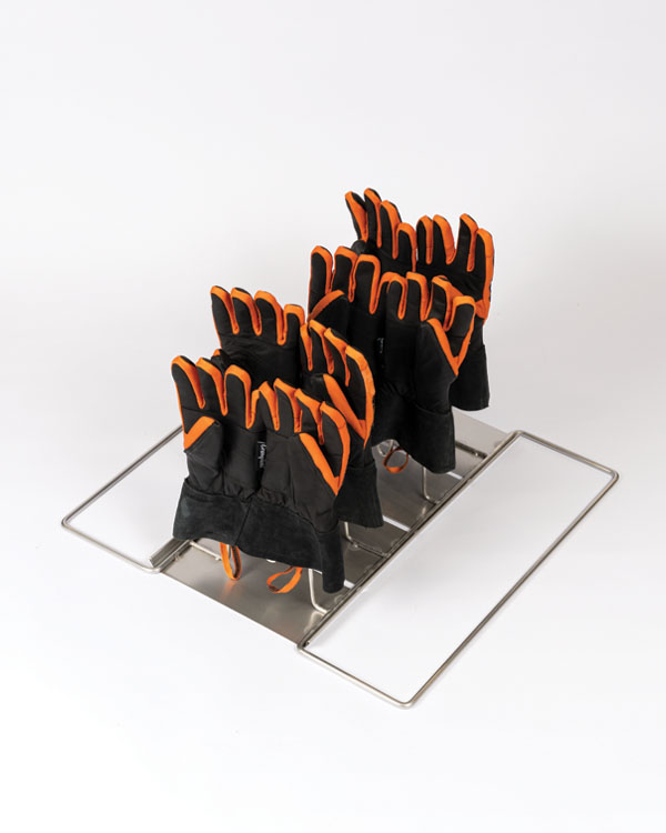 Support métallique avec base rectangulaire, tenant quatre paires de gants de pompier noirs avec bordure orange, disposés debout en deux rangées.