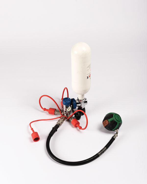 Insert de pression avec bouteille d'air blanche, tuyaux rouge et noir, et raccords utilisés pour prévenir l’humidité dans les valves respiratoires.