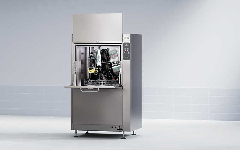 Öppen dekontamineringsmaskin i rostfritt stål med brandutrustning inuti, kontrollpanel på höger sida.