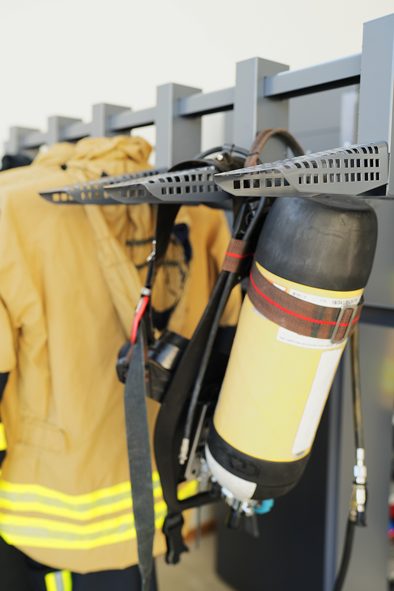 Firefighting gear on a rack, including yellow-black SCBA, face mask, and turnout gear with reflective stripes.
